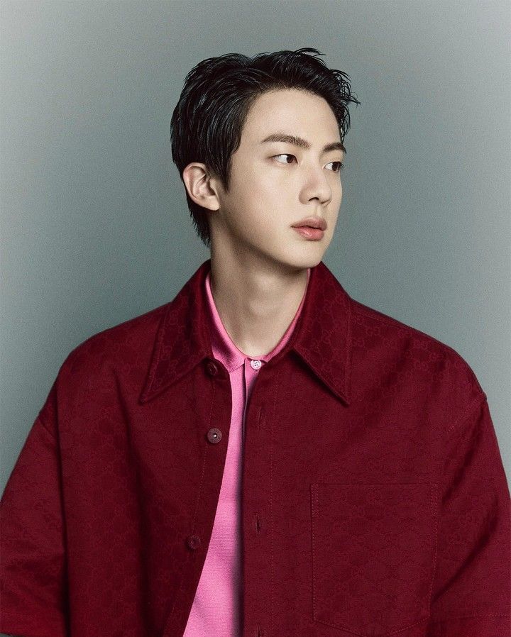 Jin of BTS wearing a red Gucci jacket and pink shirt, showcasing his role as a global fashion icon and brand ambassador.