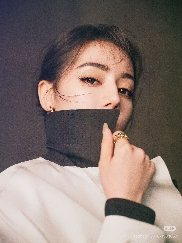 Close-up portrait of Dilraba Dilmurat in a high-collar jacket with gold rings, striking a fashionable and mysterious pose for a modern editorial shoot.