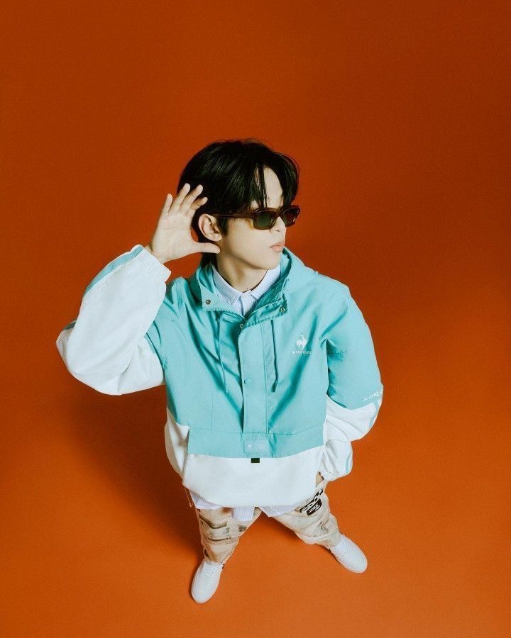 Korean rapper Big Naughty posing in a mint green windbreaker against an orange background, showcasing streetwear fashion