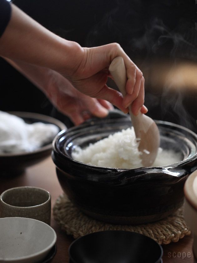 Person scooping freshly steamed Japanese rice from a traditional donabe clay pot during home meal preparation